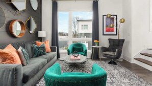 Una sala de estar moderna con un sofá gris, sillones color turquesa, una mesa de centro y un ventanal con cortinas.
