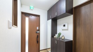 A hallway with a wooden door, a wall-mounted thermostat, and a small plant on a shelf. - OYADO - Self Check-In Only (Osaka)