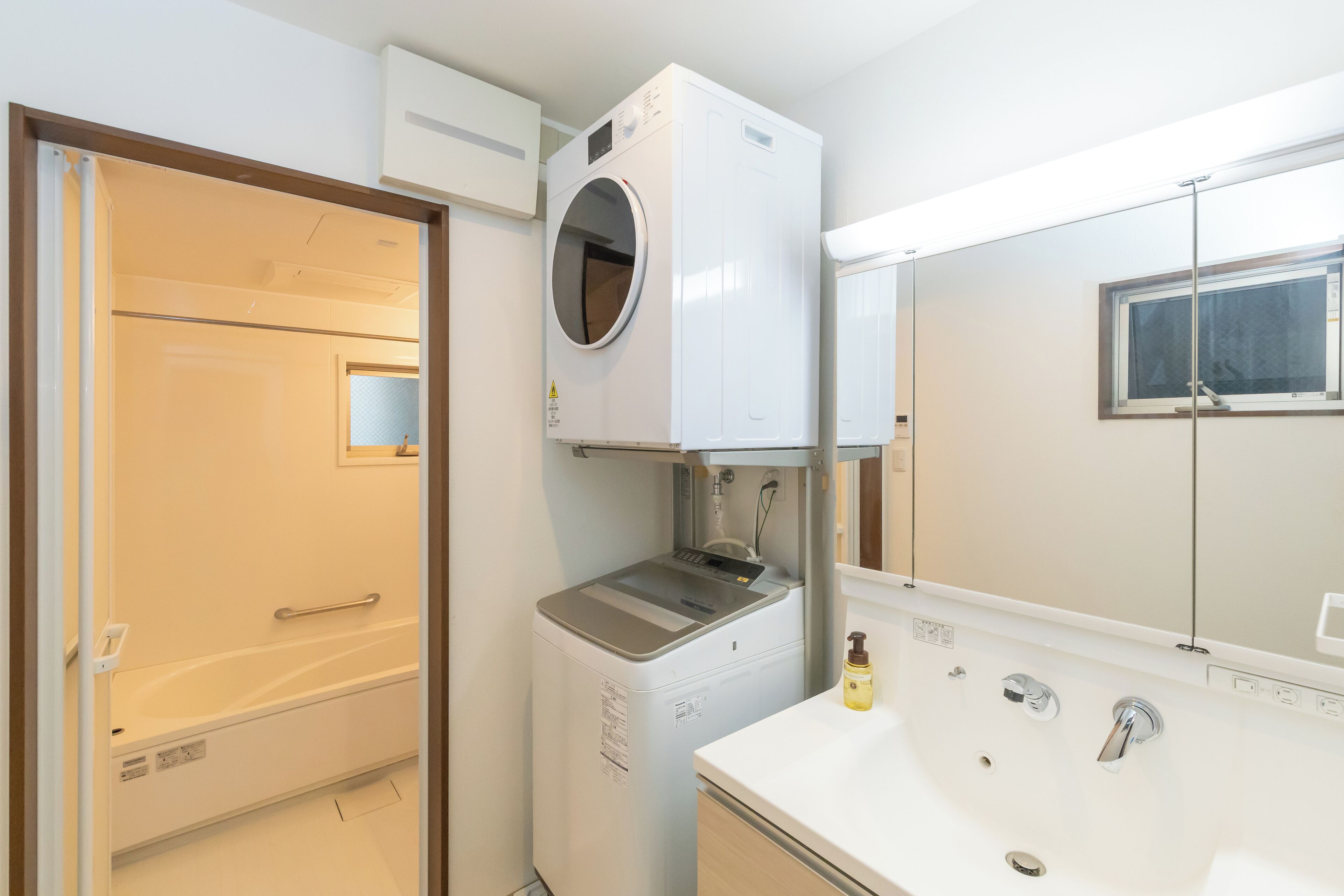 A compact bathroom with a built-in washing machine, a bathtub, and a sink with a mirror.