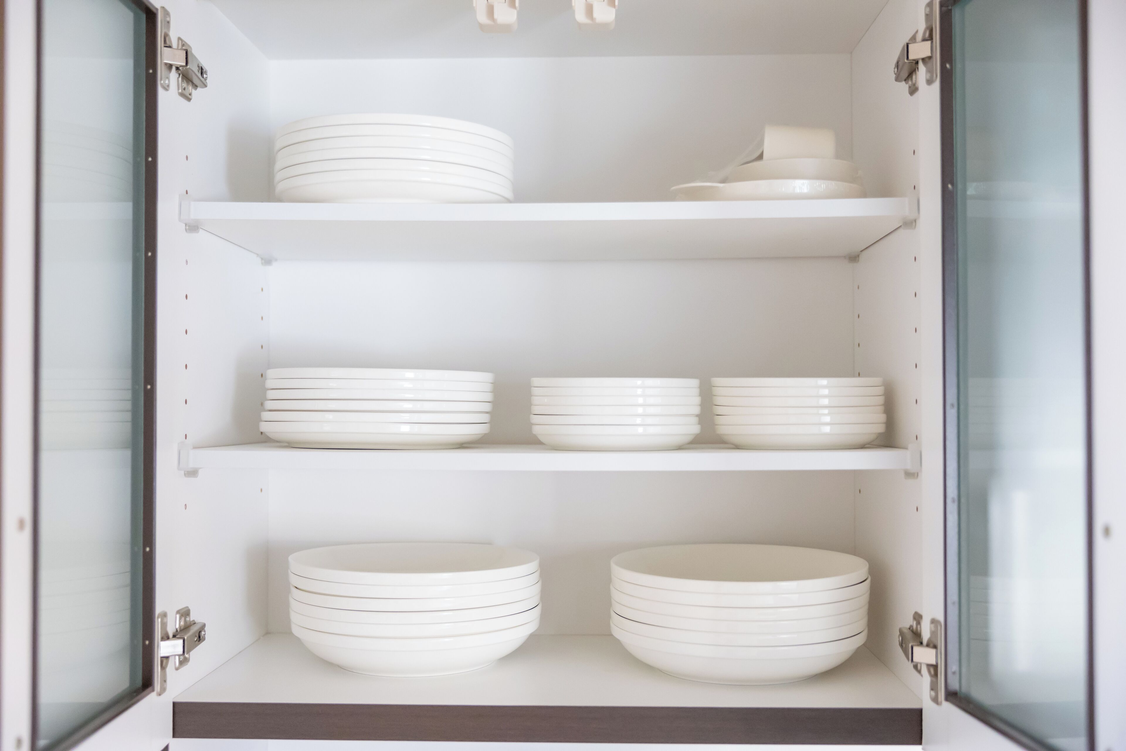 A kitchen cabinet with white shelves holding stacked plates and bowls.