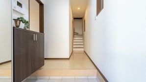 A narrow hallway with a wooden cabinet and a plant on the left, a staircase in the center, and a white wall on the right. - OYADO - Self Check-In Only (Osaka)