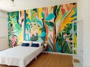 A bedroom with a large tropical-themed mural on the wall, a bed with white bedding, and a bedside table with a lamp. - Bright, Spacious, and Well-Connected: Your Perfect Retreat in Rome (Roma)