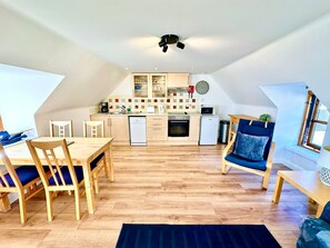Une cuisine compacte dotée d’appareils électroménagers modernes, un coin repas avec des meubles en bois et une grande fenêtre qui laisse entrer la lumière naturelle.