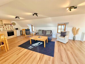 Un vaste espace de vie doté d’un plancher en bois, d’un canapé, d’un fauteuil, d’une table basse et d’une cuisine à l’arrière-plan.