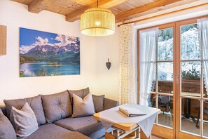 Une pièce chaleureuse avec un canapé, une table, un tableau représentant un lac de montagne et une vue sur un paysage enneigé par la fenêtre.