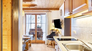 A compact kitchen with wooden cabinets, a built-in stove, and a dining area with a table and chairs. - Apartment 'Höllental' with Mountain View, Balcony, and Wi-Fi (Grainau)