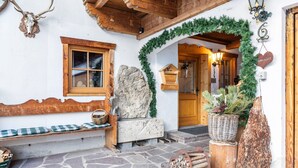 A rustic exterior with a stone bench, wooden beams, a stone wall, and a wooden door. - Apartment 'Höllental' with Mountain View, Balcony, and Wi-Fi (Grainau)