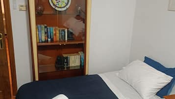 Un dormitorio con cama, almohadas, una mesita de noche y un armario de madera con libros.