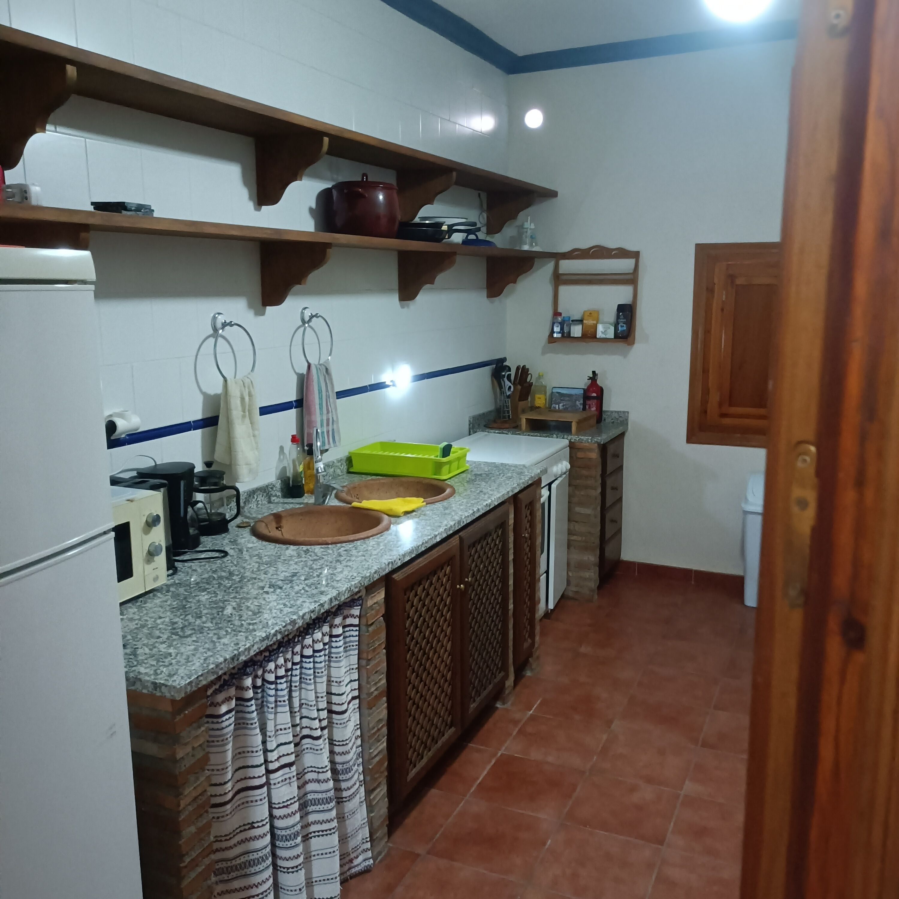 A kitchen with granite countertops, two sinks, wooden cabinets, and a tiled backsplash.