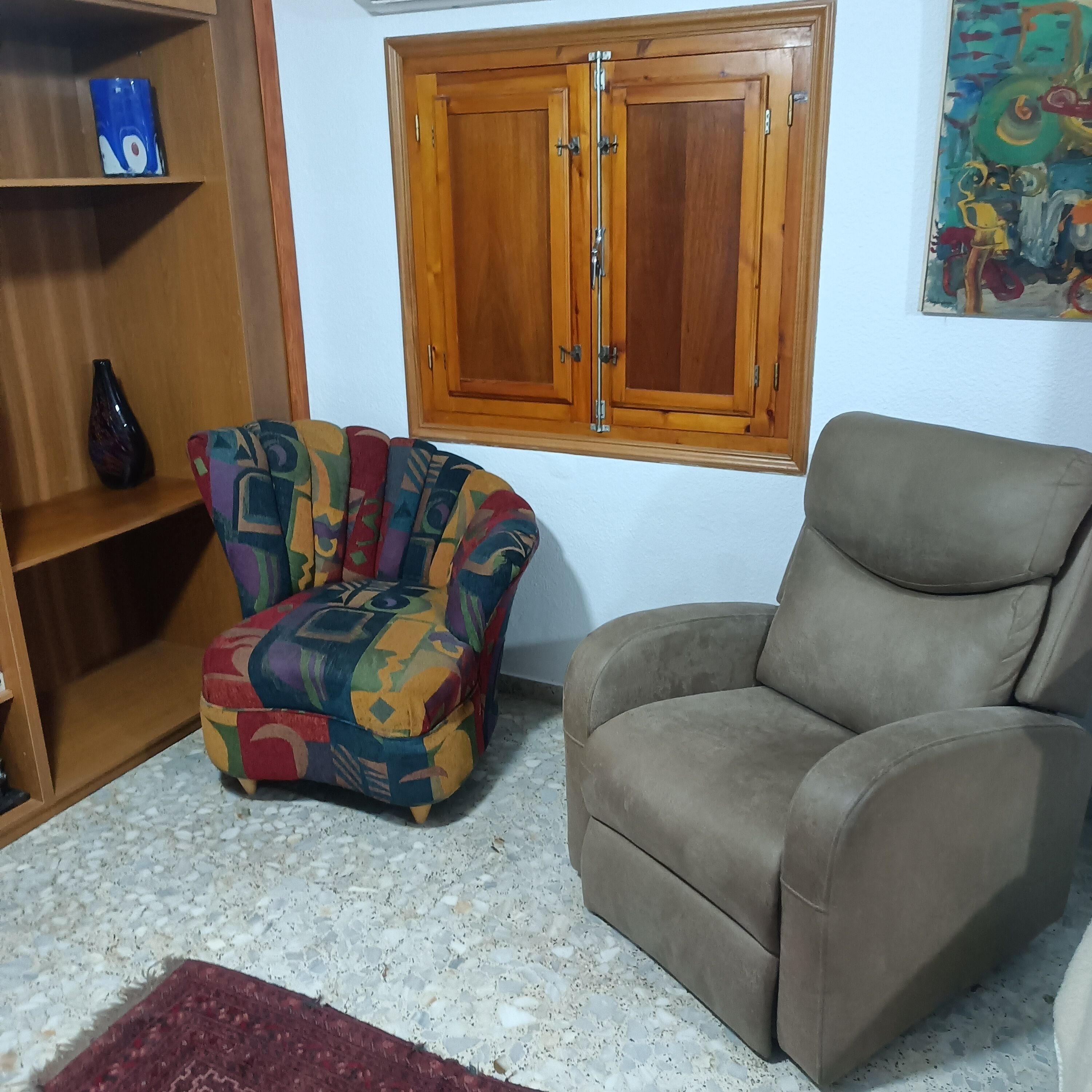 Un salon comprenant un fauteuil à motifs, un fauteuil uni, un meuble en bois et un tableau accroché au mur.