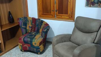 Un salon comprenant un fauteuil à motifs, un fauteuil uni, un meuble en bois et un tableau accroché au mur.