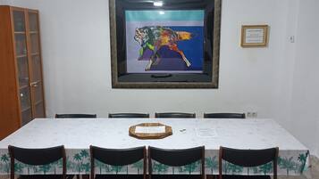 Een eethoek met een lange tafel, zes stoelen en een kunstwerk erboven.