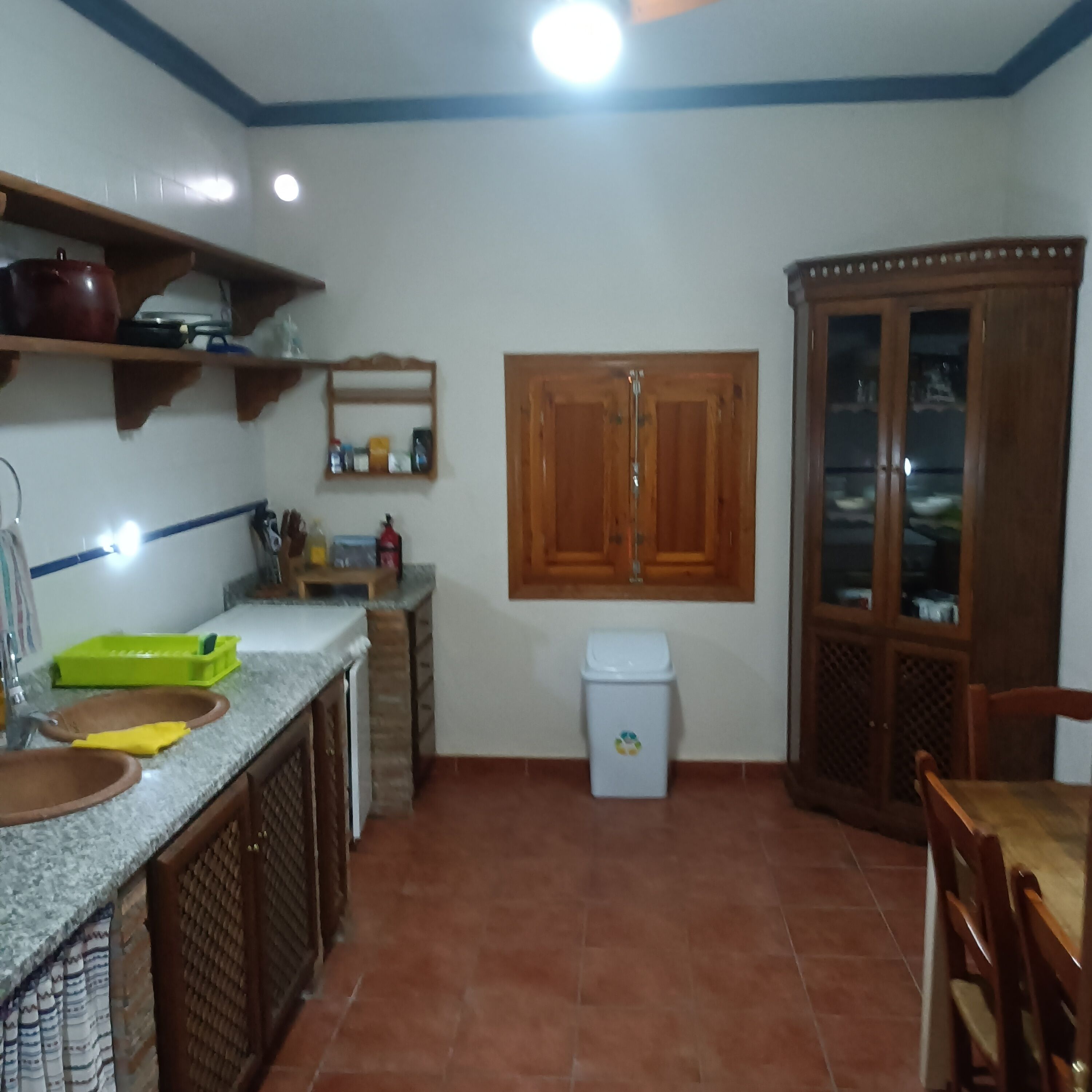 A kitchen with a granite countertop, a sink, a trash bin, and wooden cabinets.