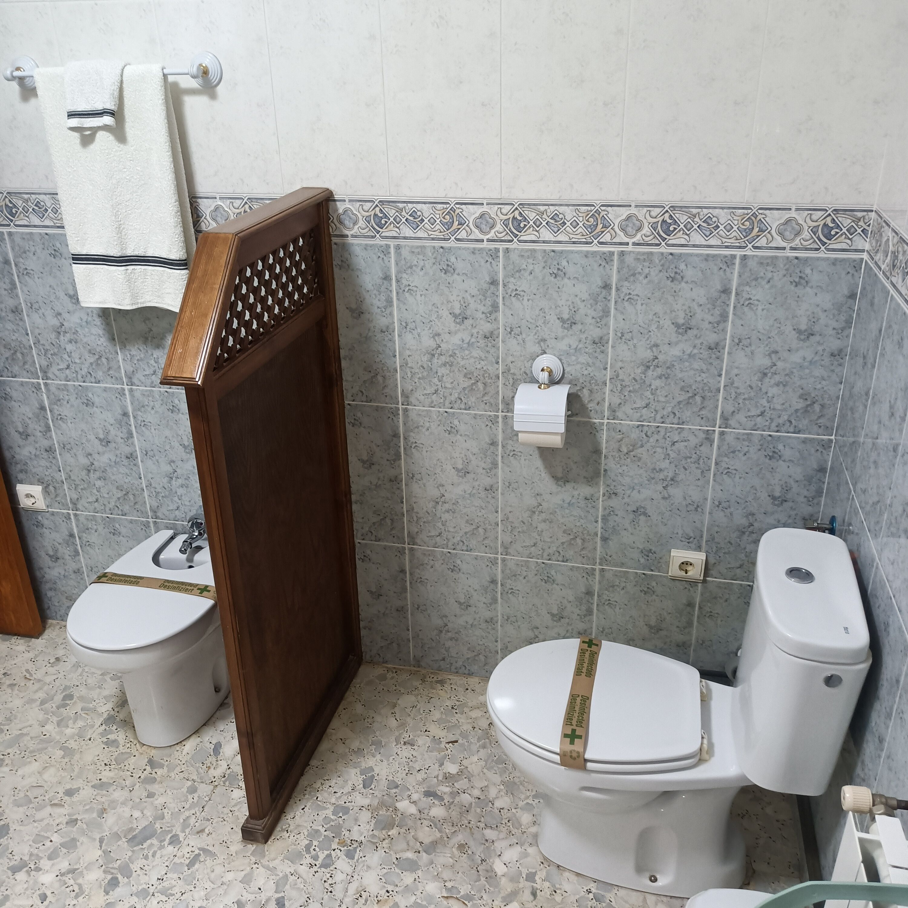 A bathroom with two toilets, a towel rack, and a decorative tile border.