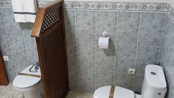 A bathroom with two toilets, a towel rack, and a decorative tile border.