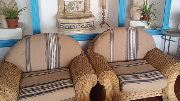 Une pièce comprenant deux fauteuils en osier, un mur recouvert de carreaux avec une fontaine décorative, et une statue.