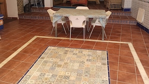 Un coin repas avec une table dressée pour quatre personnes, entourée de chaises, et un tapis à motifs sur le sol.