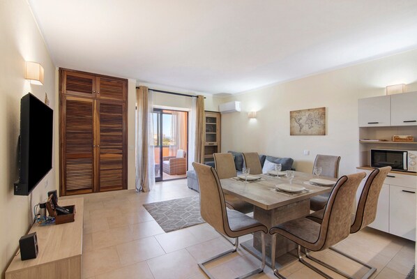 Una sala moderna con comedor, televisor y puerta corrediza de vidrio que da a un balcón.