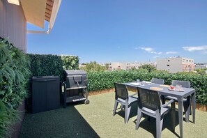 Un patio con una mesa, sillas, una parrilla y una planta en maceta.