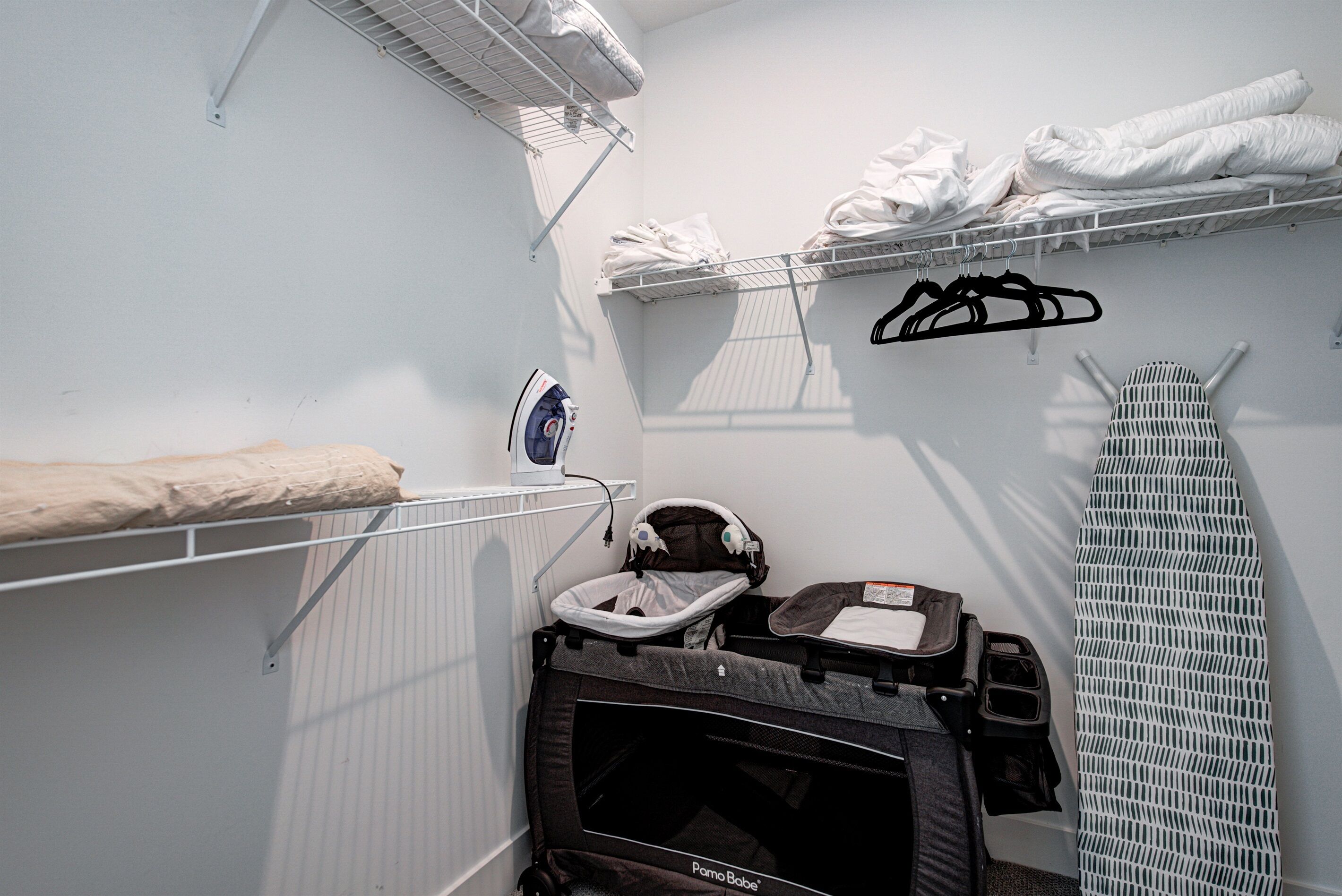 A laundry area with a drying rack, ironing board, and a baby stroller.