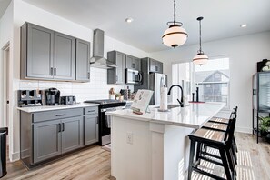 A modern kitchen with grey cabinets, a central island, and pendant lighting. - Stylish Luxury Rooftop Home (Indianapolis)