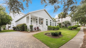 A white two-story house with a covered porch, a brick driveway, and well-maintained lawns. - IndiGo Blue- Golf Cart! Pool & Fitness Center (Santa Rosa Beach)