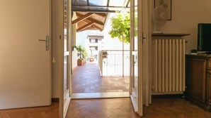 Une porte ouverte donnant sur un balcon d’où l’on peut admirer un immeuble et un arbre.