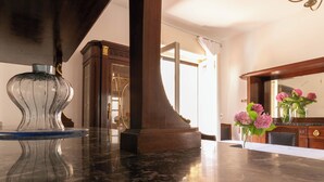 Un hall d’accueil en marbre, agrémenté d’un vase en verre, d’une armoire en bois et d’un miroir qui reflète des fleurs roses.