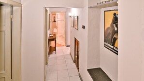 A hallway with a tiled floor, a wooden door, a small table, and a poster on the wall. - Corte Dei Portici - Three Bedroom Apartment, Sleeps 6 (Lucca)