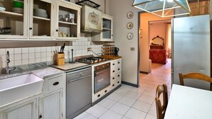 A kitchen with white cabinets, a stove, a sink, and a dining area with a table and chairs. - Corte Dei Portici - Three Bedroom Apartment, Sleeps 6 (Lucca)