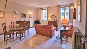 A living room with a glass dining table, red upholstered sofa, and a small round table with a lamp. - Corte Dei Portici - Three Bedroom Apartment, Sleeps 6 (Lucca)