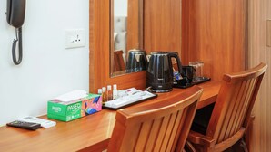 A wooden table with a phone, a box of tissues, a coffee maker, and a remote control. - Royal Plaza City (Kozhikode)