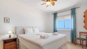 Une chambre d’hôtel avec un lit, une table de chevet avec une lampe, une chaise en bois et une fenêtre avec des rideaux.