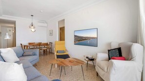Un salon comprenant un canapé, une table basse, un fauteuil, un téléviseur et un tableau représentant un paysage.