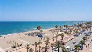 Une vue sur la plage, avec une large promenade, des palmiers et un ciel bleu dégagé.