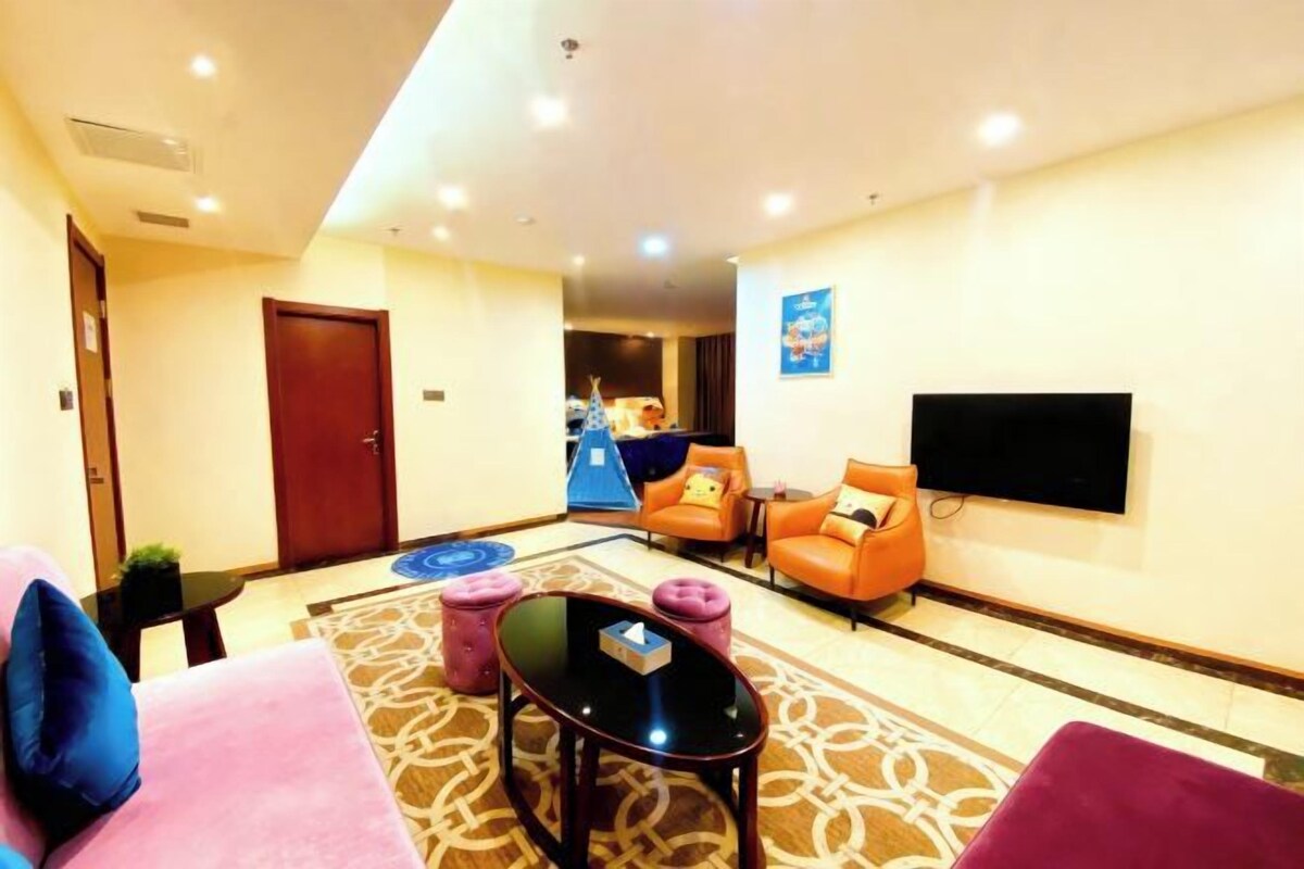 A hotel lobby with a sofa, chairs, a coffee table, a flat-screen TV, and a patterned rug.