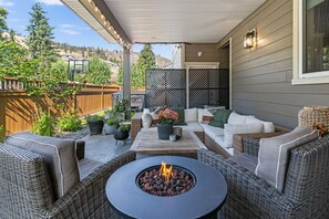 An outdoor patio with wicker furniture, a central fire pit, and a view of a hilly landscape.