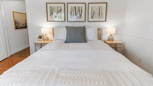 A neatly arranged bedroom with a large bed, two bedside tables with lamps, and three framed artworks on the wall.
