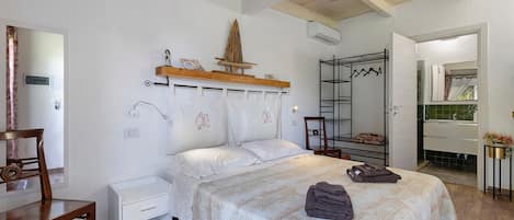 A bedroom with a bed, a chair, a bedside table, a wooden shelf with decorative items, and a wardrobe with a mirror.