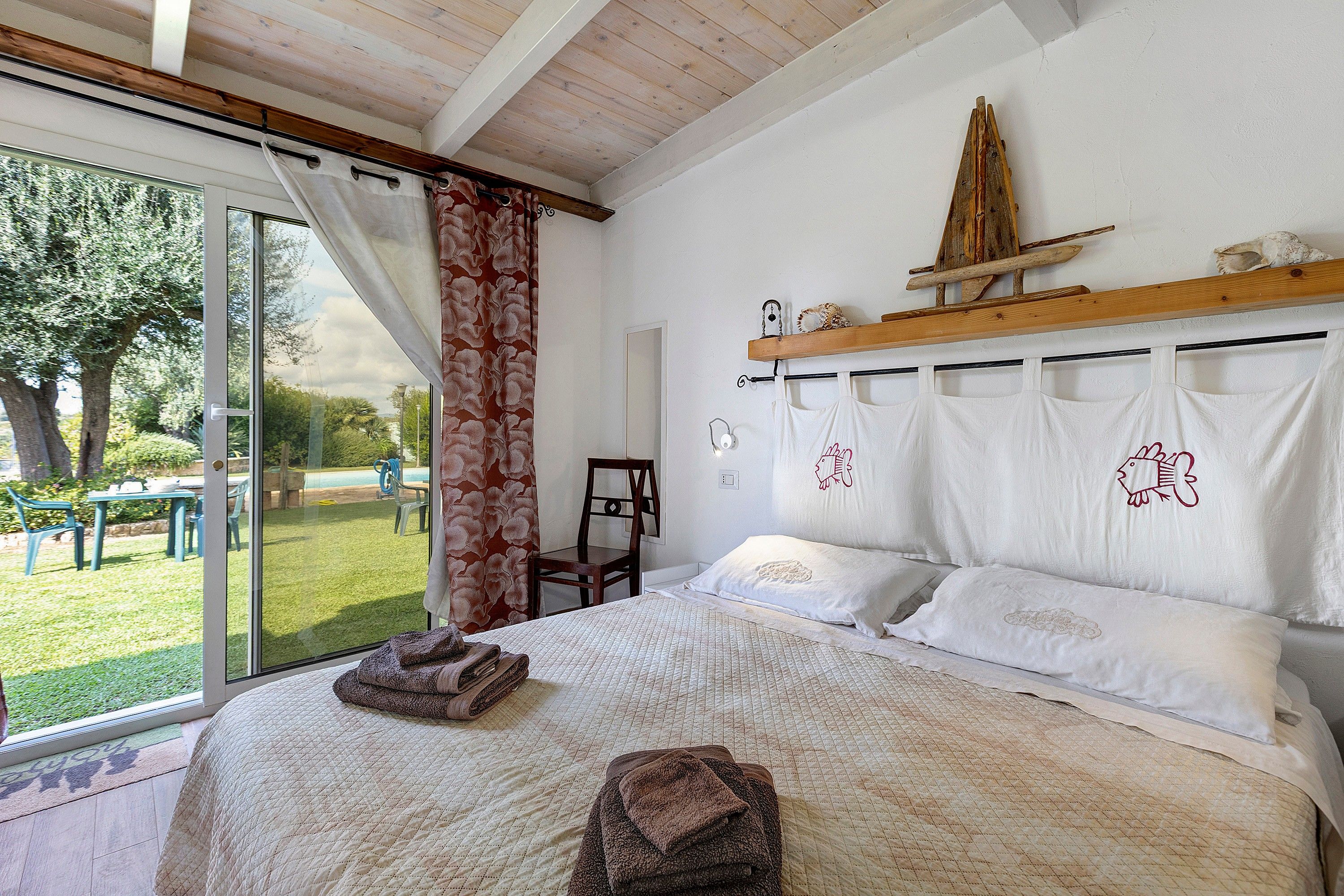 Quarto com cama grande, cabeceira de madeira, janela com cortinas e vista para o exterior.