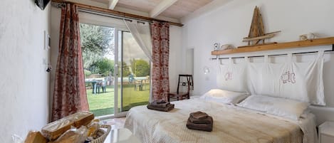 A bedroom with a large bed, a wooden headboard, a basket of bread, and a view of the outdoors.