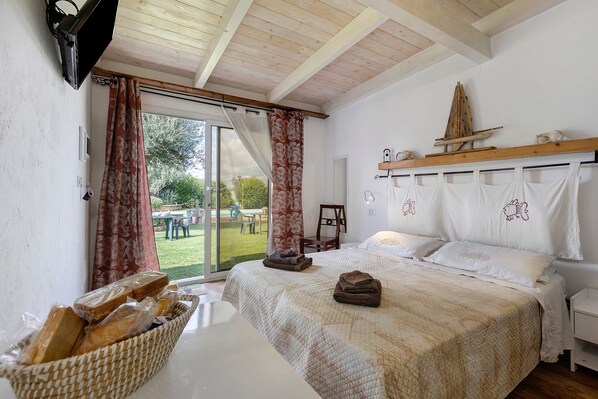 A bedroom with a large bed, a wooden headboard, a basket of bread, and a view of the outdoors.