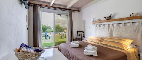 A bedroom with a bed, a table with a bowl of snacks, a chair, and a view of the outdoors through a sliding door.