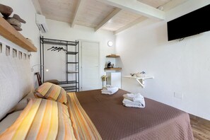 A bedroom with a bed, a wardrobe, a mirror, a shelf with towels, and a mounted TV. - Apartment 'Mirto' with shared pool, Wi-Fi and air conditioning (Alghero)