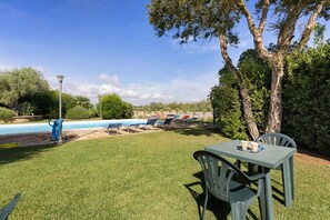 A pool area with lounge chairs and a table, surrounded by grass and trees. - Apartment 'Rosmarino' with shared pool, Wi-Fi and air conditioning (Alghero)