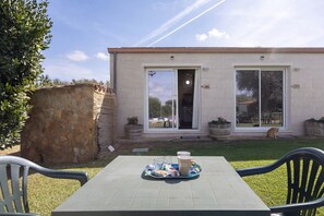 A patio with a table set for two, a stone wall, and a house with a sliding glass door. - Apartment 'Rosmarino' with shared pool, Wi-Fi and air conditioning (Alghero)