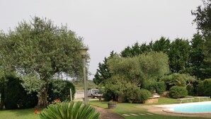 A stone pathway leading to a swimming pool, surrounded by lush greenery and a variety of trees. - Apartment 'Rosmarino' with Shared Pool, Wi-Fi and Air Conditioning (Alghero)