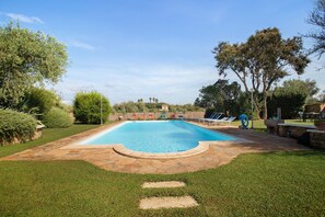A rectangular swimming pool with a surrounding stone deck, surrounded by a well-maintained lawn and various trees. - Apartment 'Rosmarino' with shared pool, Wi-Fi and air conditioning (Alghero)