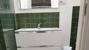 A bathroom with a white sink, green tiles, and a trash bin. - Apartment 'Rosmarino' with Shared Pool, Wi-Fi and Air Conditioning (Alghero)