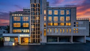 Een modern hotelgebouw met een opvallende cilindervormige constructie, veel ramen en een goed verlichte entree.